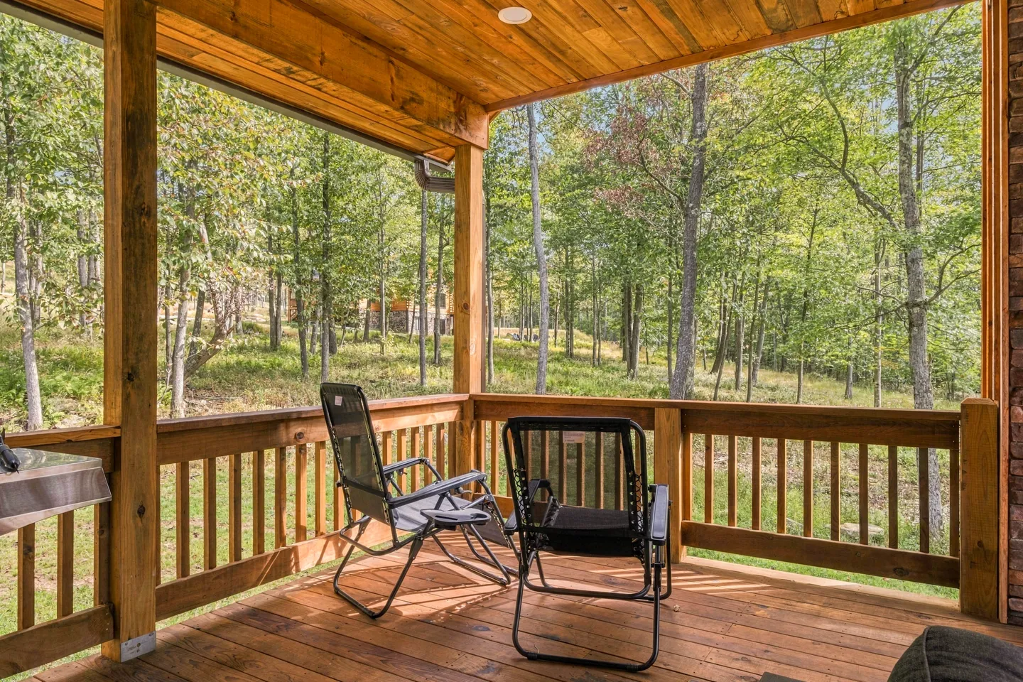 A covered wooden porch with folding chairs overlooking a wooded area.
