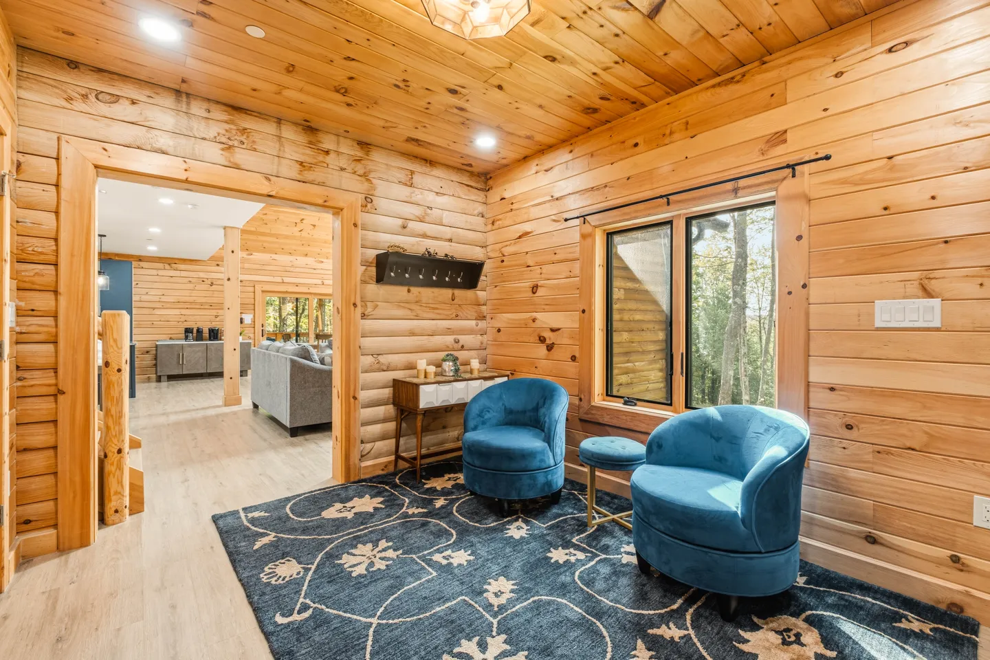 Seating area in a log cabin interior featuring two blue velvet armchairs, a patterned blue rug, and pine wood walls.
