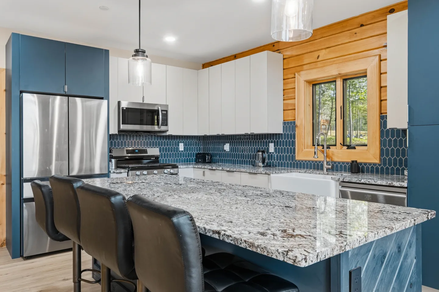 Kitchen with large granite island, bar stools, blue honeycomb tile backsplash, and stainless steel appliances.