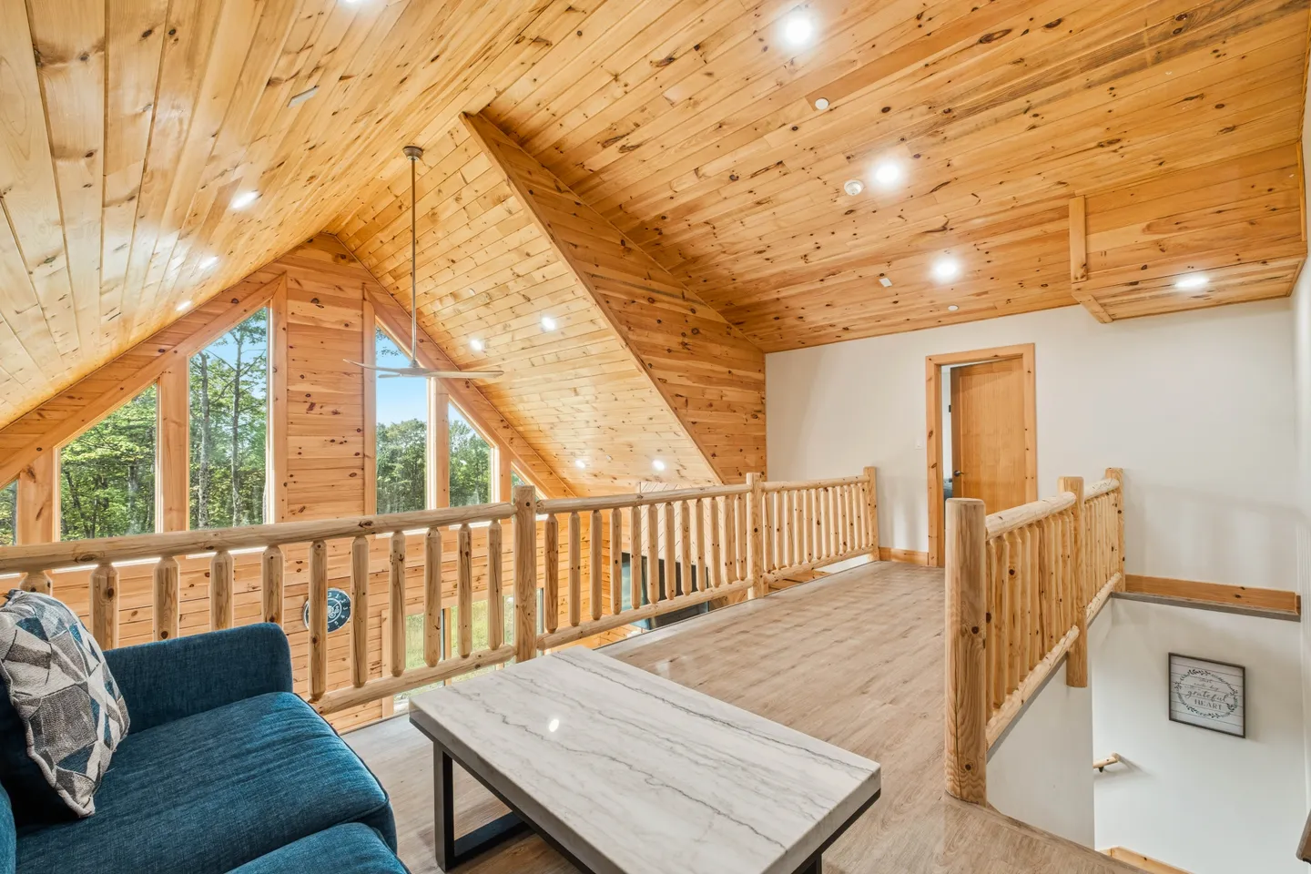 Upstairs loft with knotty pine vaulted ceilings, log railings, a blue sofa, and a marble-topped coffee table overlooking the floor below.