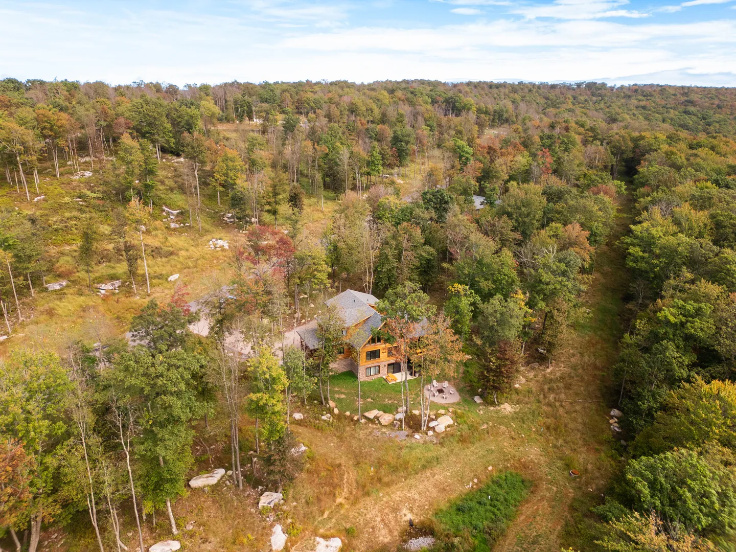 Aerial view of a multi-story cabin surrounded by dense woodland with early autumn foliage.