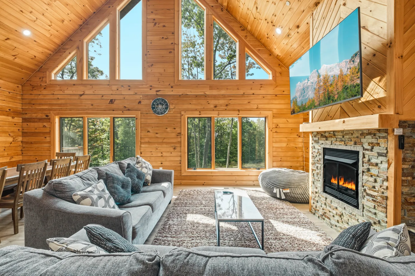 Living room with wood-paneled walls, vaulted ceiling with upper windows, stone fireplace, and gray sofa.