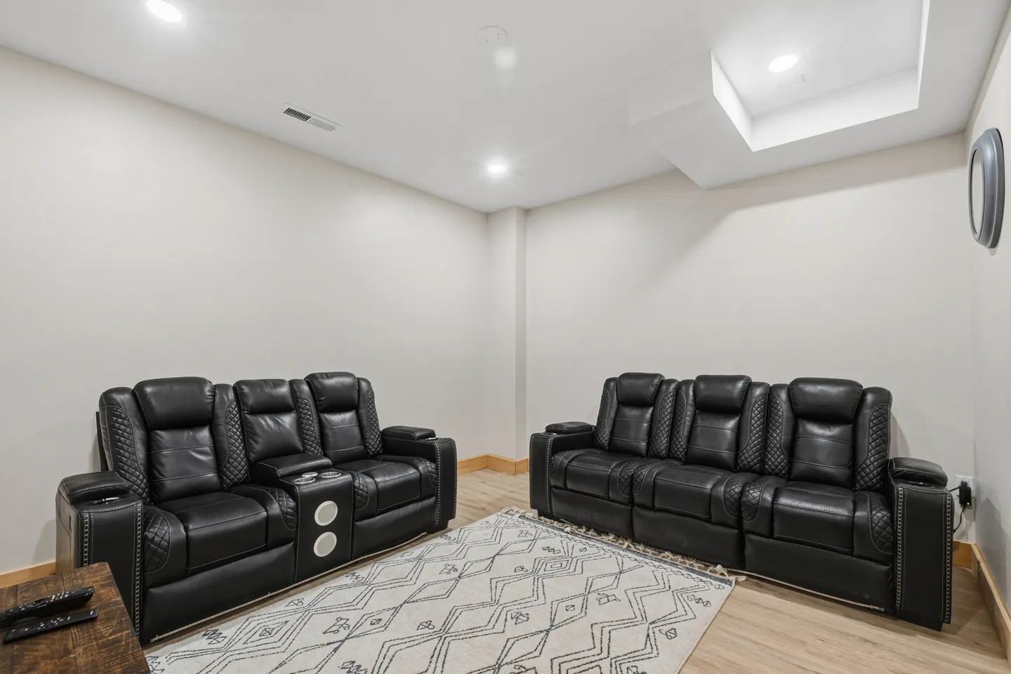 Seating area featuring two black leather reclining sofas with cup holders arranged around a patterned area rug.