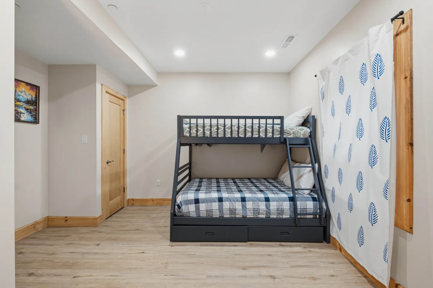 Bedroom featuring a dark gray bunk bed with built-in ladder and drawers, light wood-look flooring, and a patterned privacy curtain.