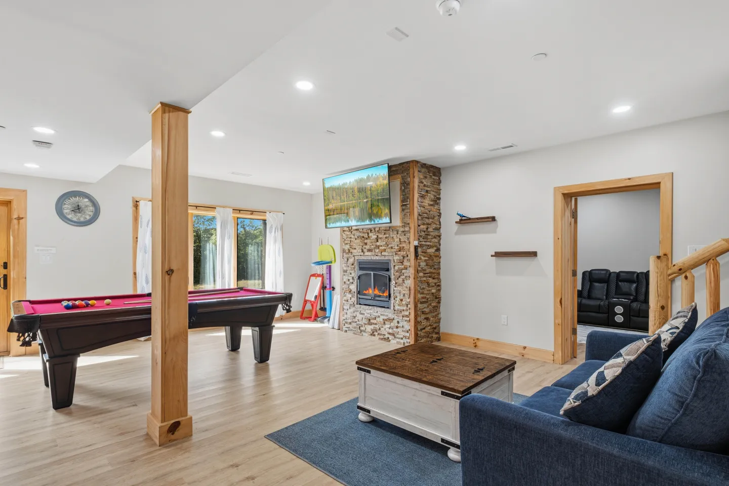 Game room featuring a red felt pool table, stone fireplace with mounted television, and a blue sofa.