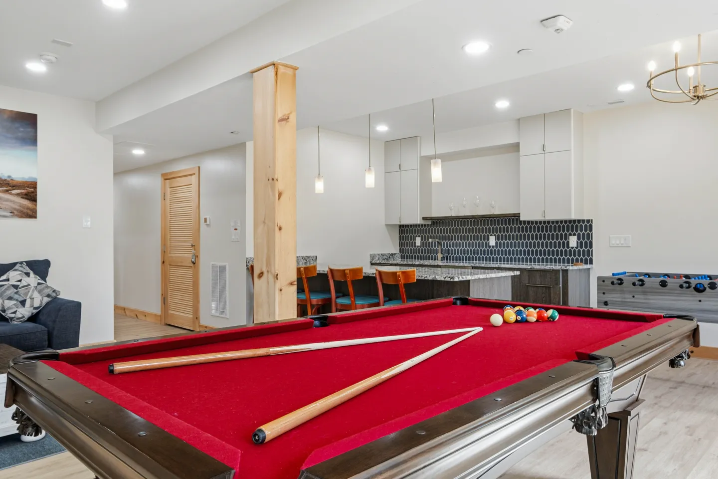 Game room featuring a red felt pool table in the foreground and a wet bar with seating in the background.