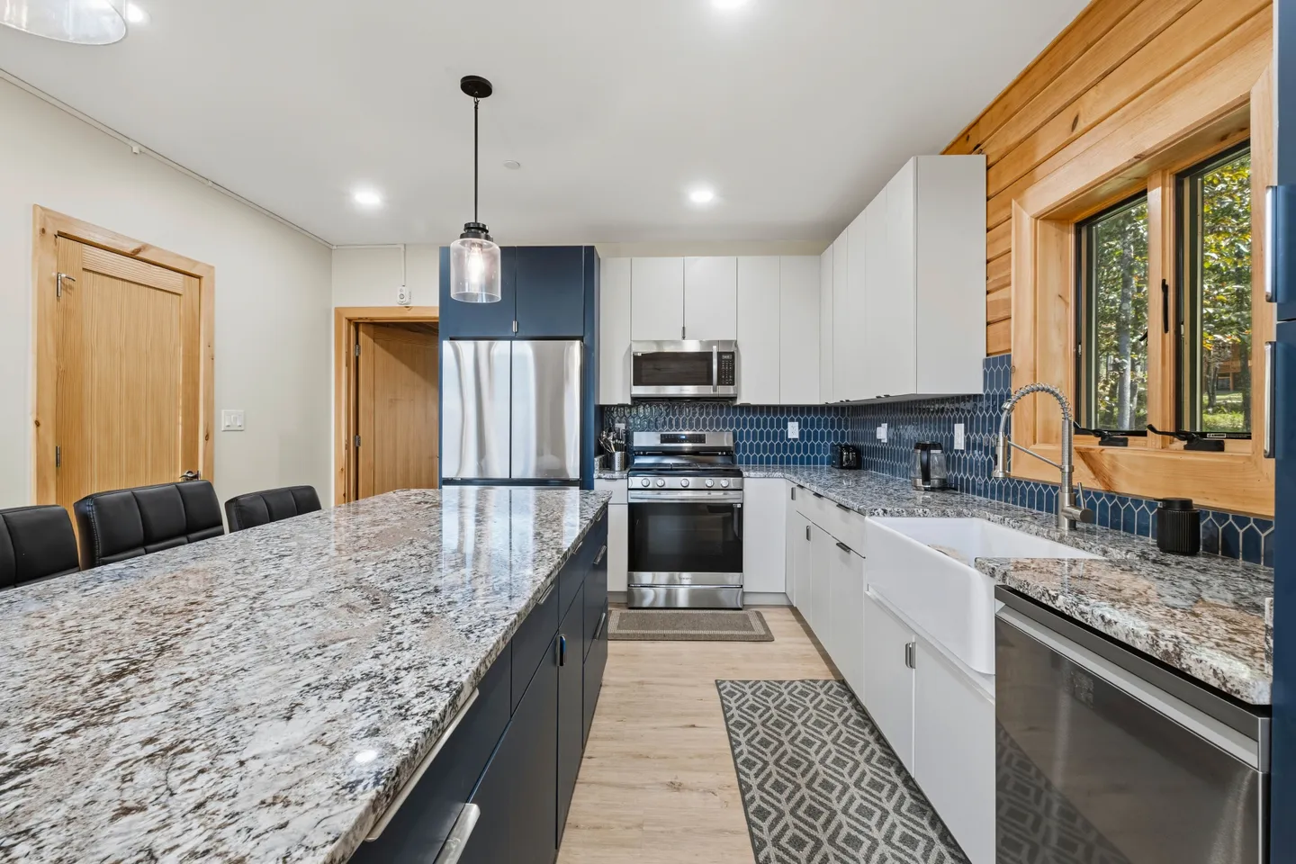 Modern kitchen with large speckled countertop island, dark blue and white cabinetry, stainless steel appliances, and a blue tile backsplash.