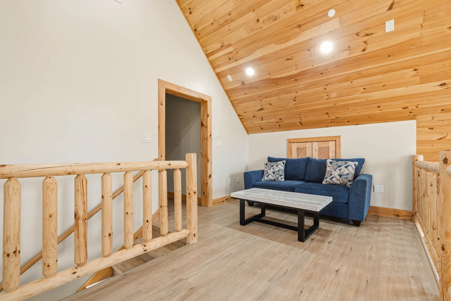 Upstairs loft landing featuring a blue sofa, light wood log railings, a coffee table, and an angled wood-plank ceiling.