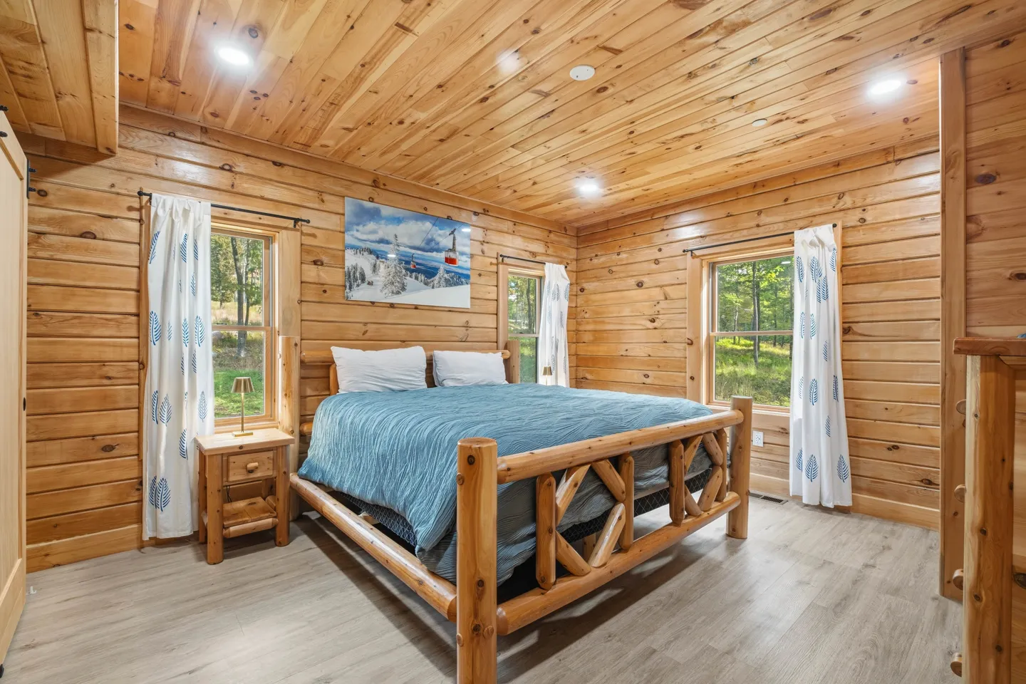 Bedroom with wood-paneled walls and ceiling, a log bed frame with a blue bedspread, and two windows.