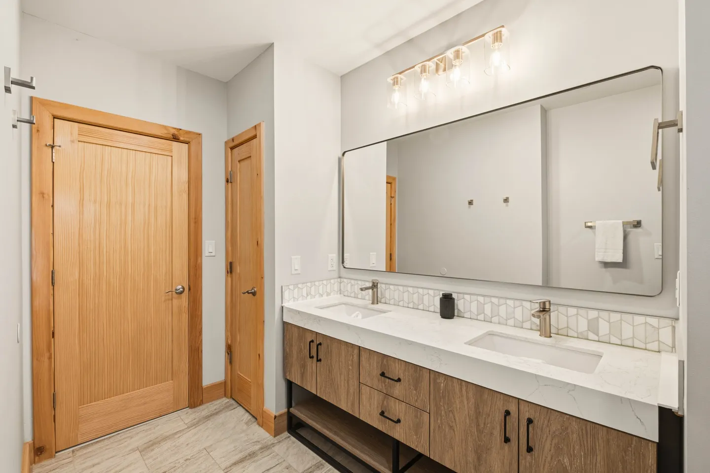 Bathroom featuring a double vanity with light countertop, wooden cabinets, a large mirror, and wood doors.