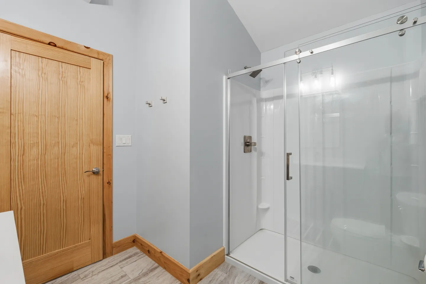 Bathroom with a wood door, light gray walls, wood baseboards, and a glass-enclosed walk-in shower with sliding door.