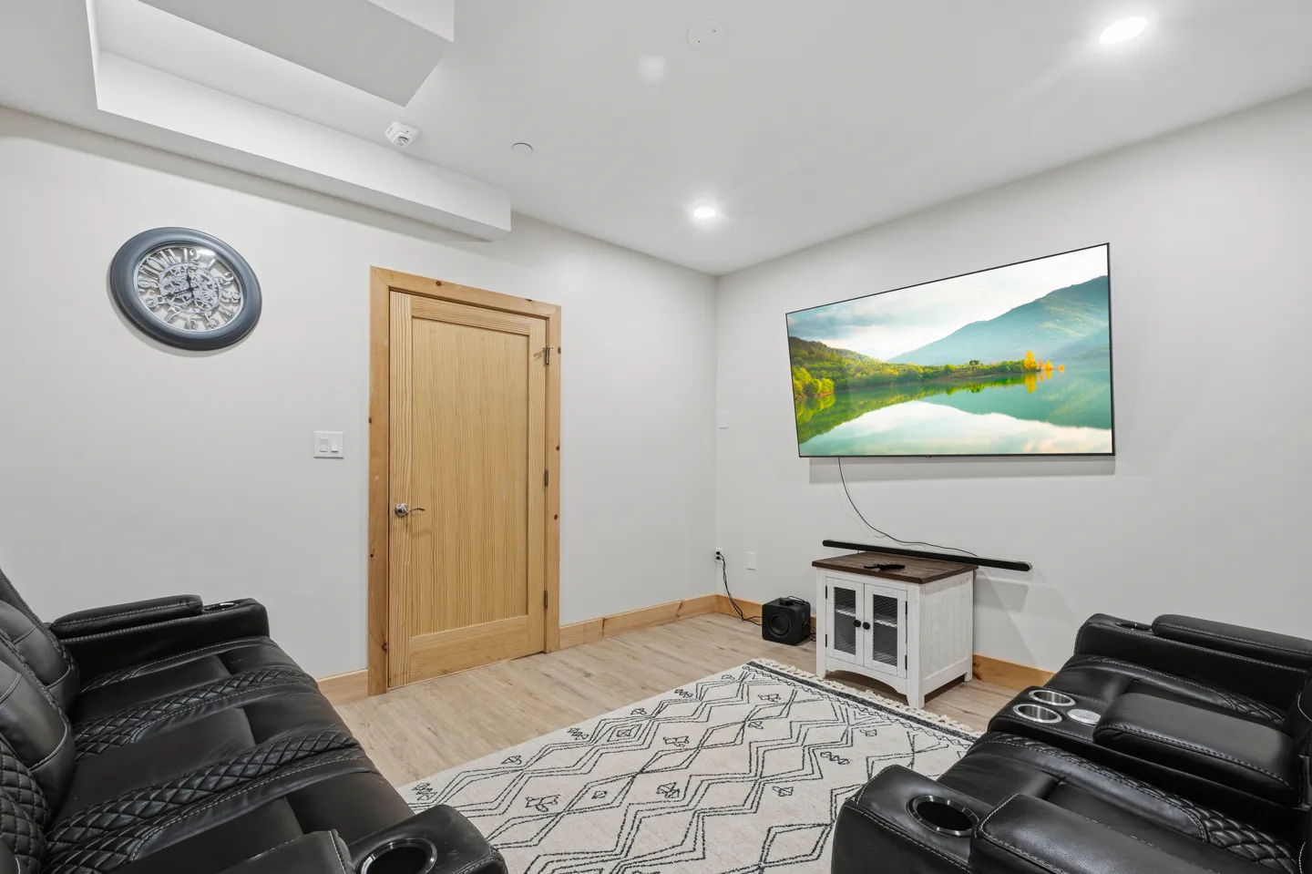 Media room with reclining black leather-style seating facing a wall-mounted TV over a small media console.