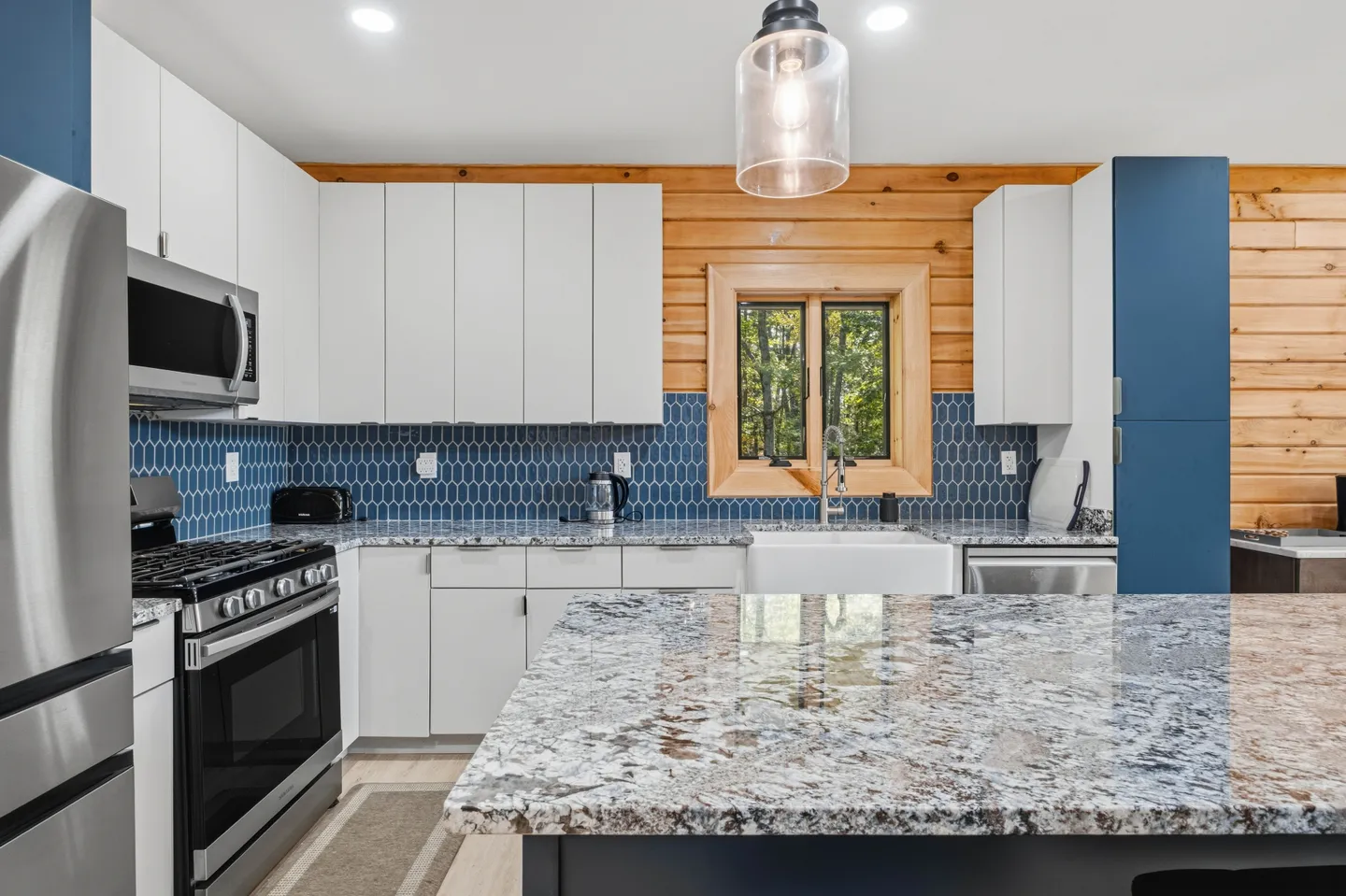 Kitchen interior featuring white cabinets, blue tile backsplash, stainless steel appliances, and a granite-topped island.