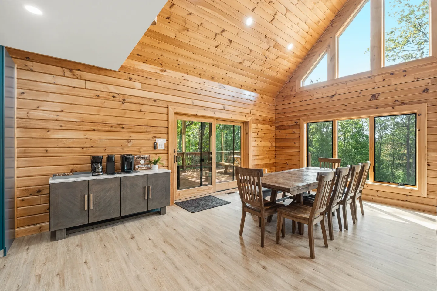 Dining area with a wooden table, chairs, vaulted wood-paneled ceiling, and sliding glass door leading to a deck.