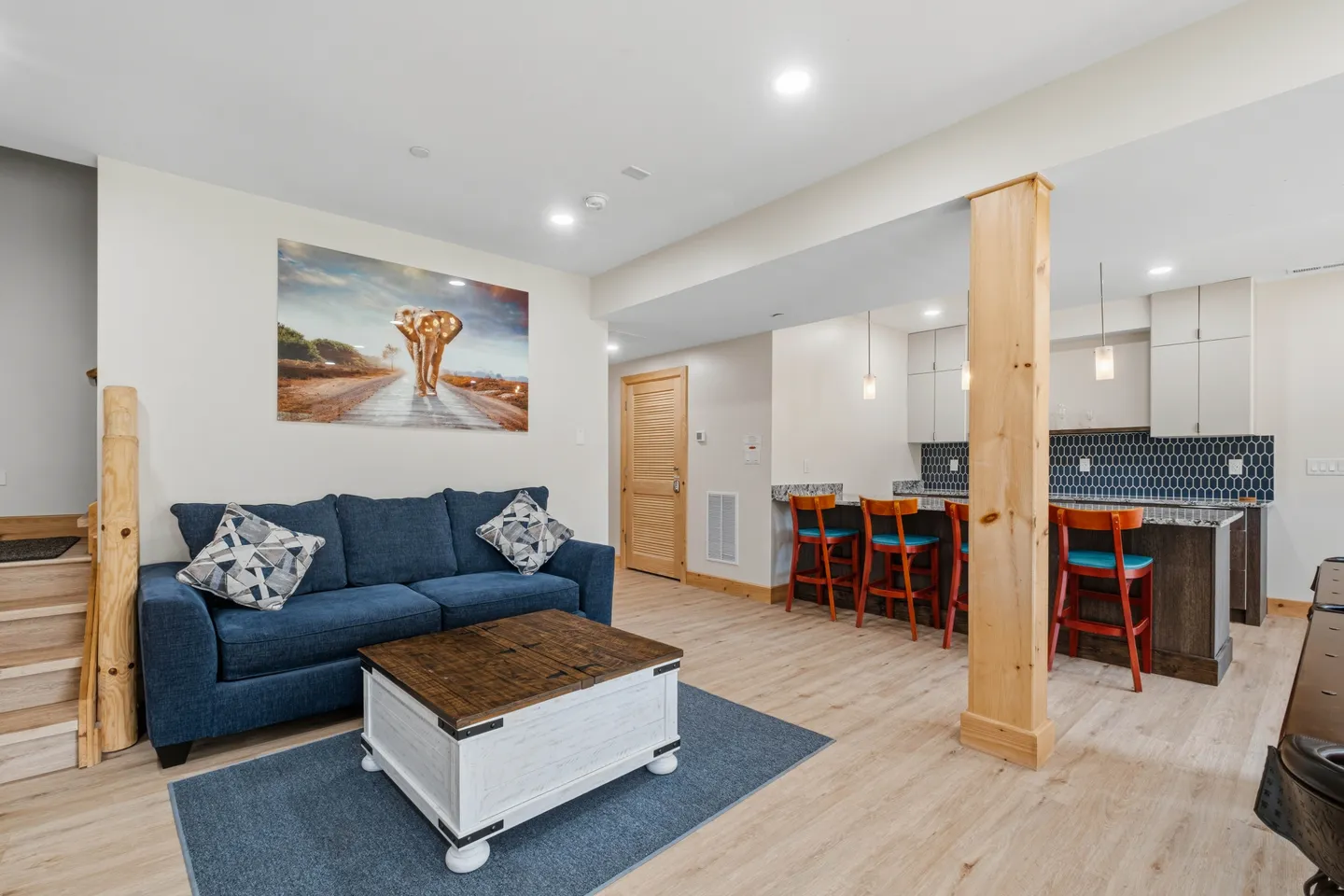 Open living area with a blue sofa, coffee table, and an adjacent kitchen with a breakfast bar and barstools.