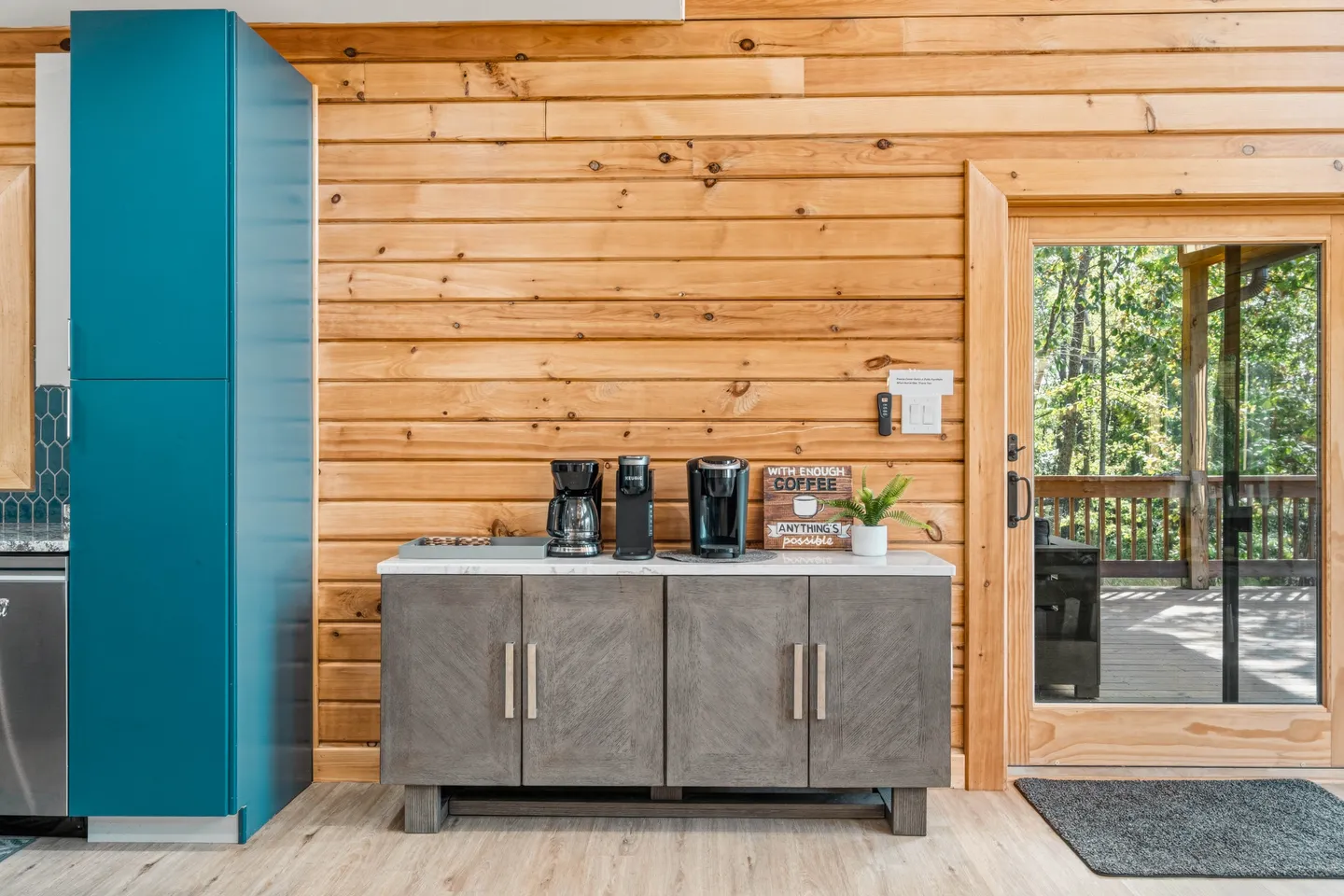 A dedicated coffee station with a gray wooden cabinet set against horizontal wood plank walls next to an exterior glass door.
