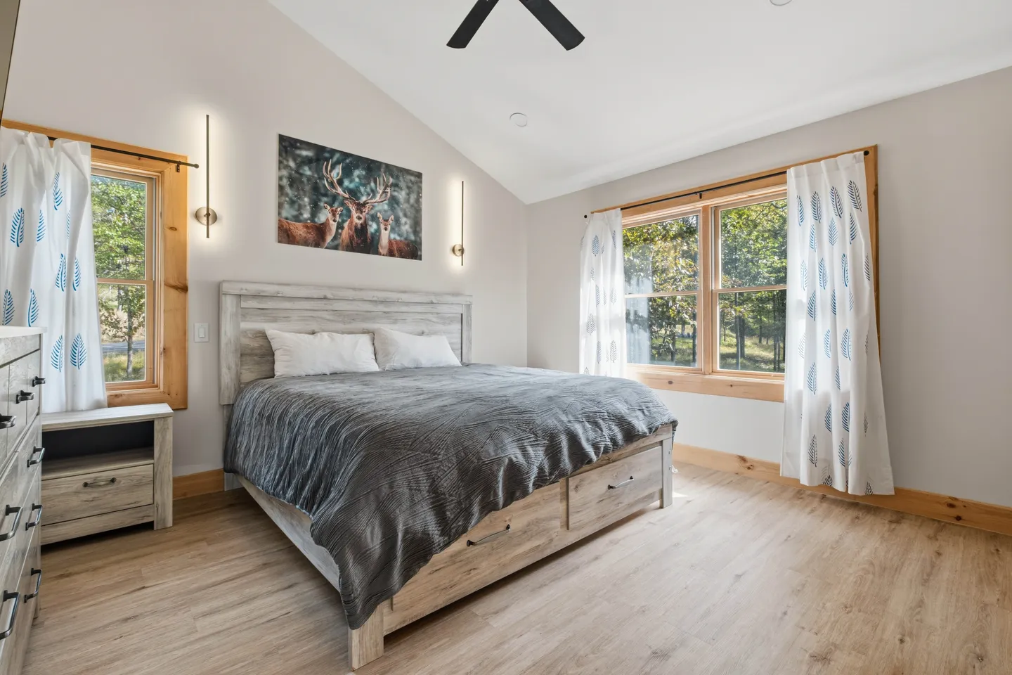 Bedroom featuring a wooden bed frame with built-in storage drawers, flanked by windows with patterned curtains.