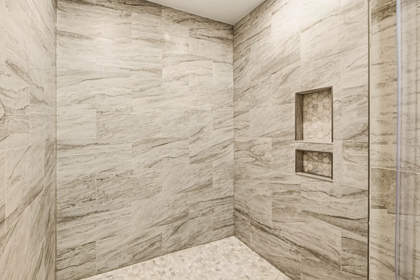 Tiled walk-in shower interior with built-in wall niche and pebble floor.