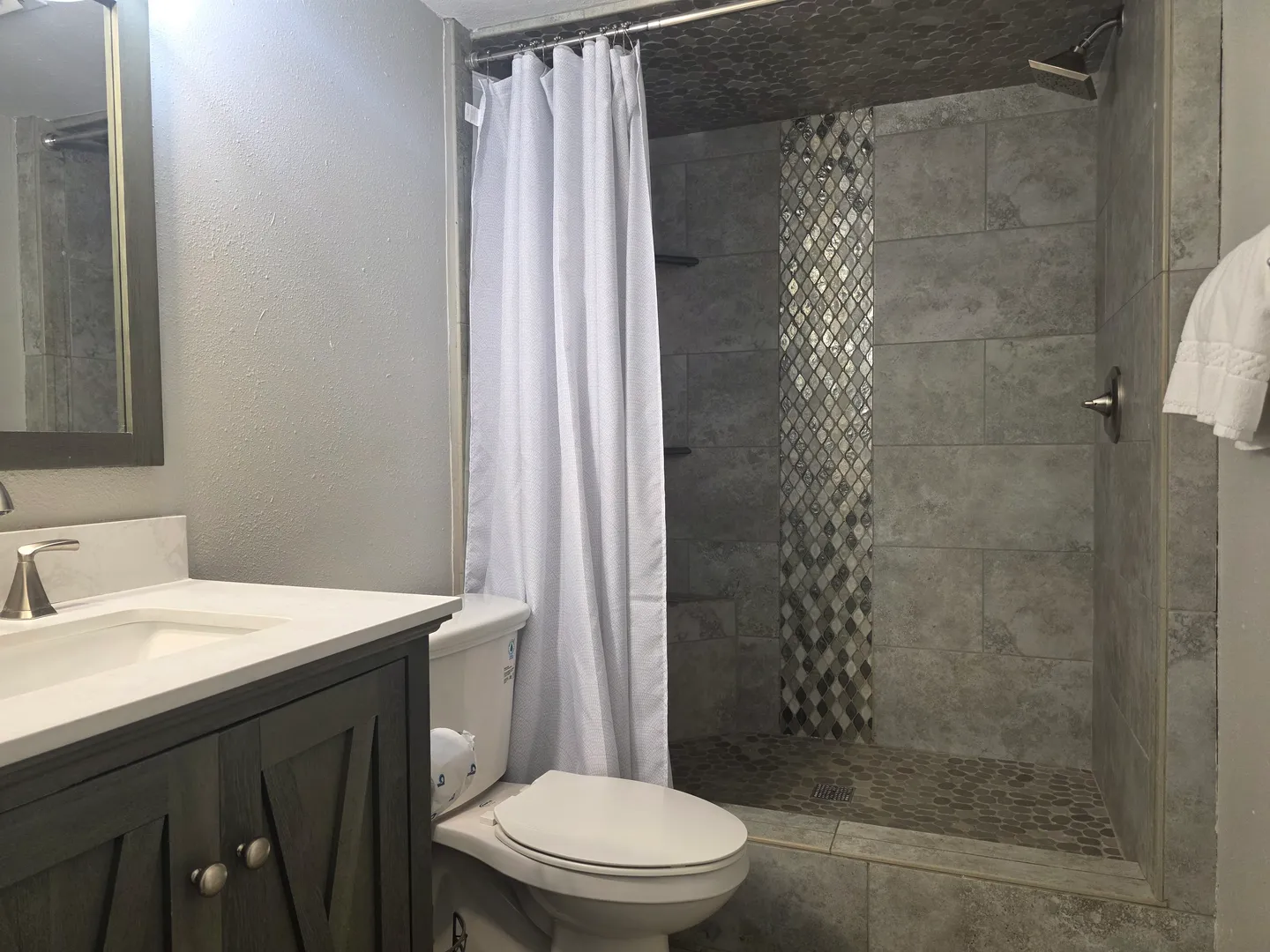 Bathroom with a vanity, toilet, and tiled walk-in shower with decorative mosaic accent.
