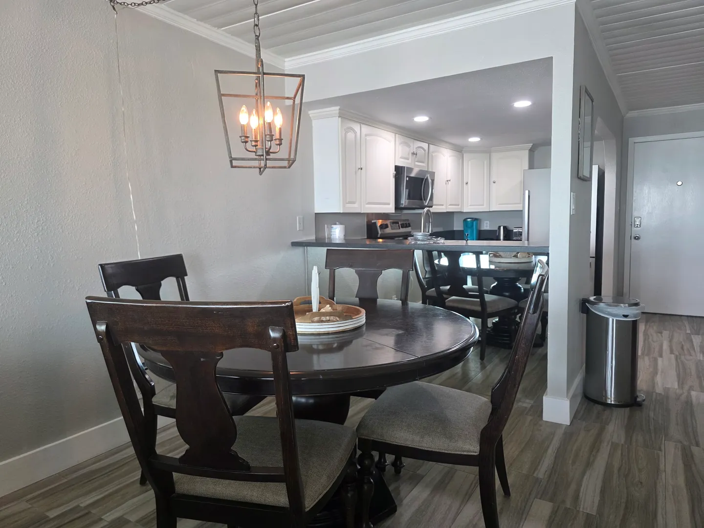 Dining area with a dark wood table and chairs situated next to an open kitchen with white cabinets.