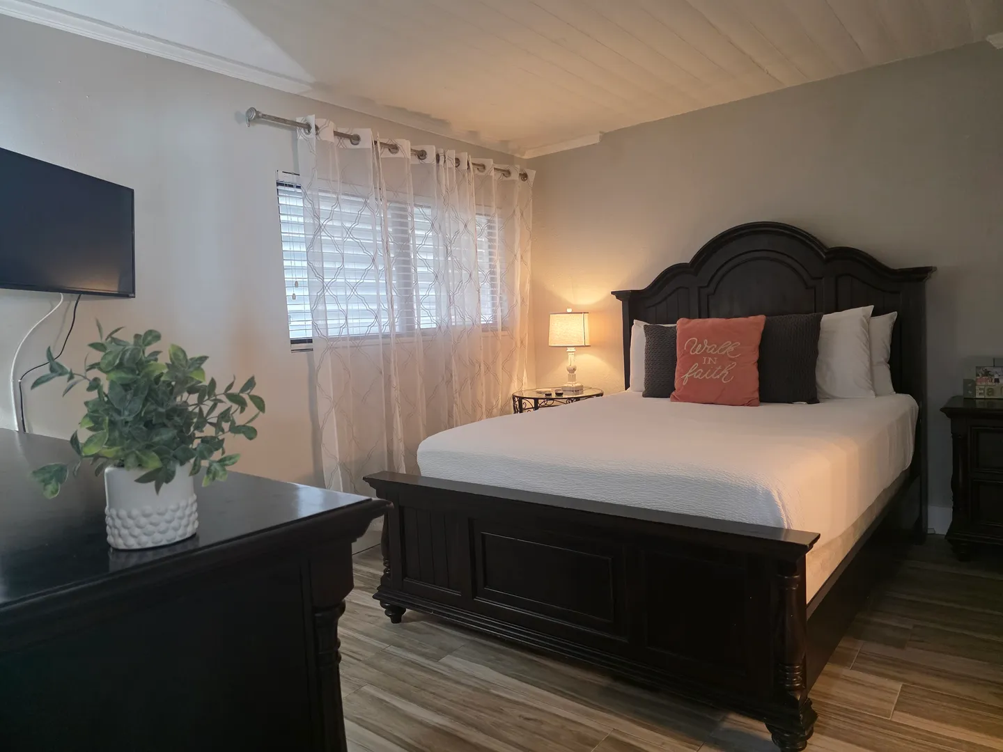Bedroom featuring a dark wood panel bed, a matching dresser with a small plant, and a wall-mounted TV.