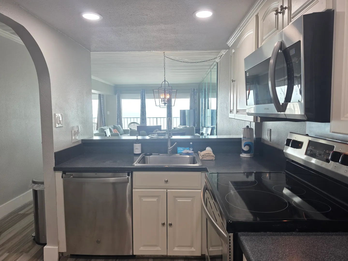 Kitchen counter with stainless steel sink, dishwasher, and stove overlooking the open-plan living room with balcony views.
