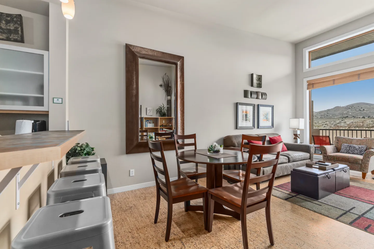 Open living and dining area featuring a round wood table, high ceilings, barstools, and views of hills through a large window.