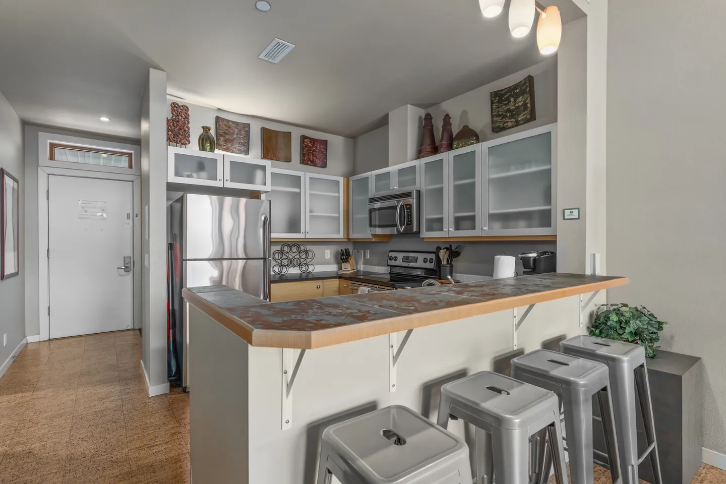 Kitchen with frosted glass front cabinets, stainless steel appliances, and a breakfast bar with metal stools.