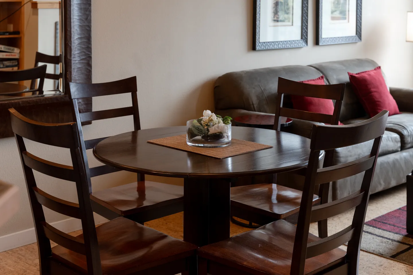 A dark wood round dining table with ladder-back chairs next to a living room couch.