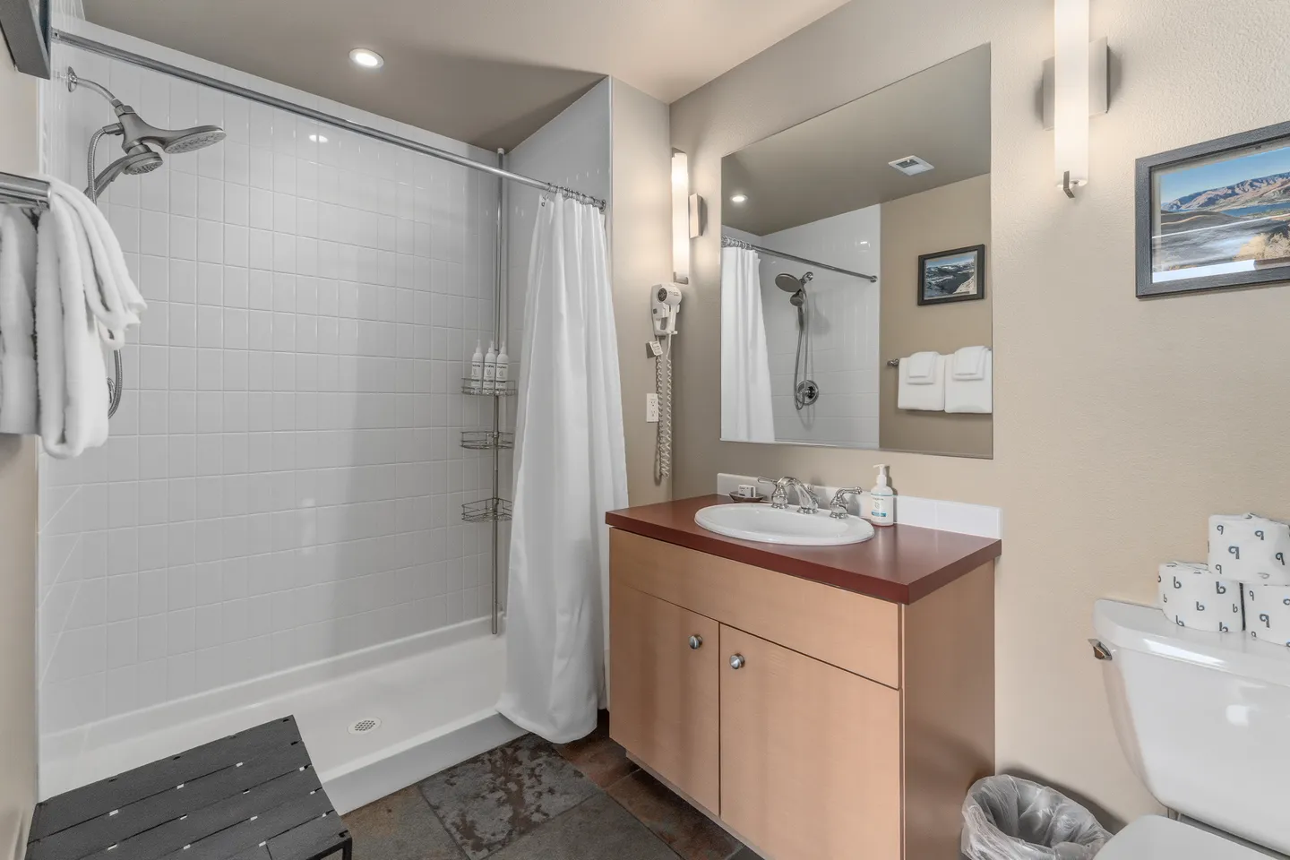Bathroom with a tiled walk-in shower, wood vanity with sink, mirror, and toilet.