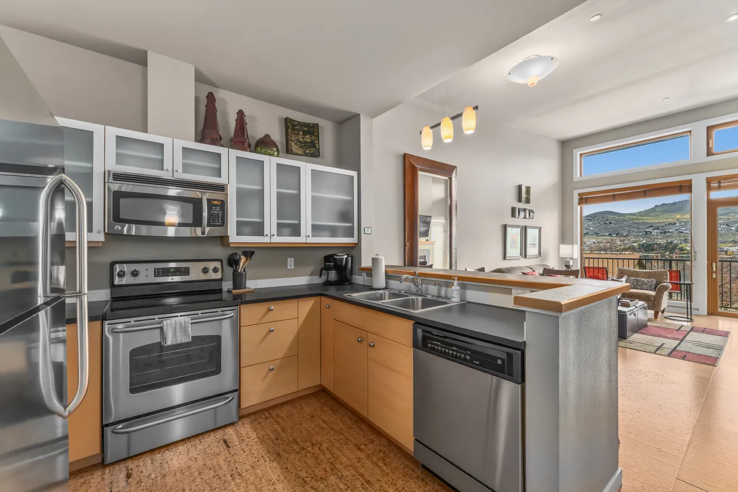 Kitchen with stainless steel appliances, light wood cabinets, and a raised breakfast bar overlooking the living area and outdoor views.