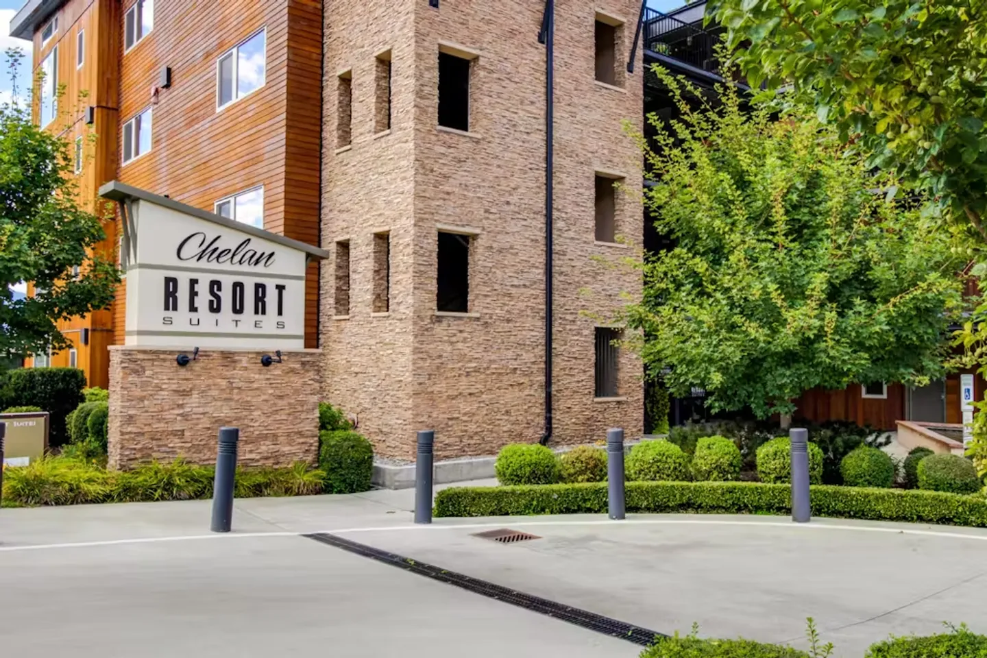 Exterior entrance sign for Chelan Resort Suites set against a multistory stone and wood-sided building.