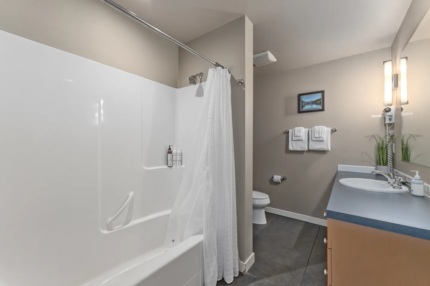Bathroom with a white bathtub and shower combination, vanity counter with sink, and toilet in the background.