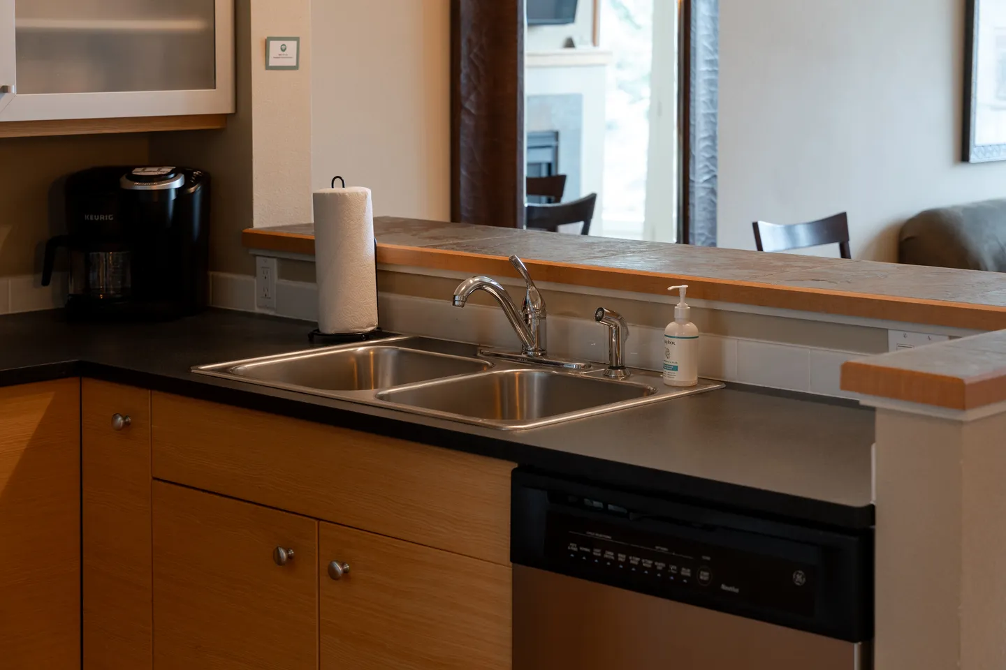 Close-up view of a kitchen counter with a double stainless steel sink, black dishwasher, and coffee maker.