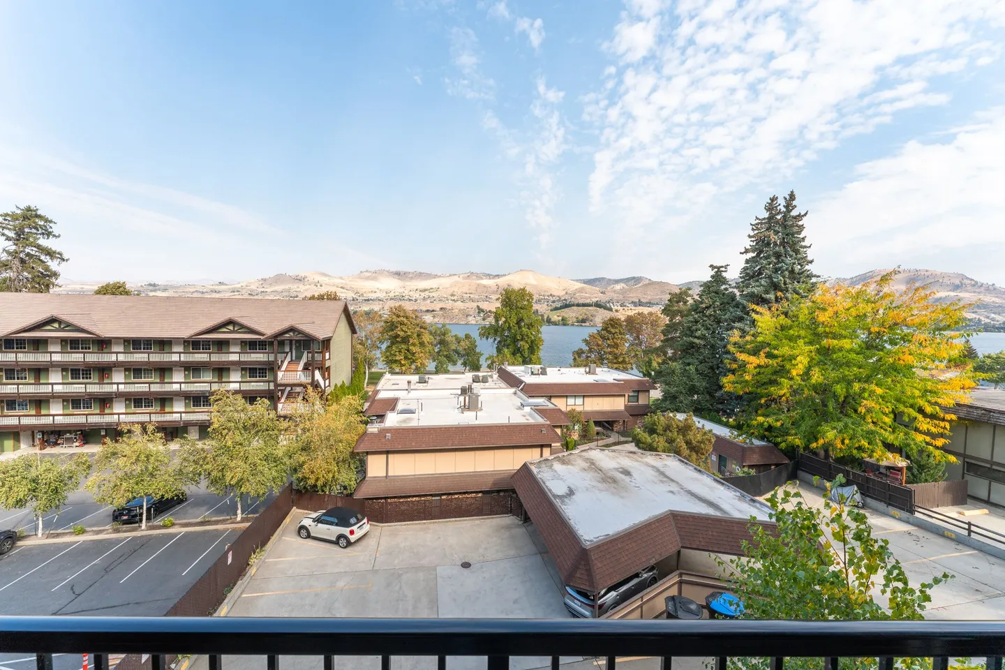 Balcony view overlooking surrounding apartment complexes, trees, a lake, and distant hills under a partly cloudy sky.