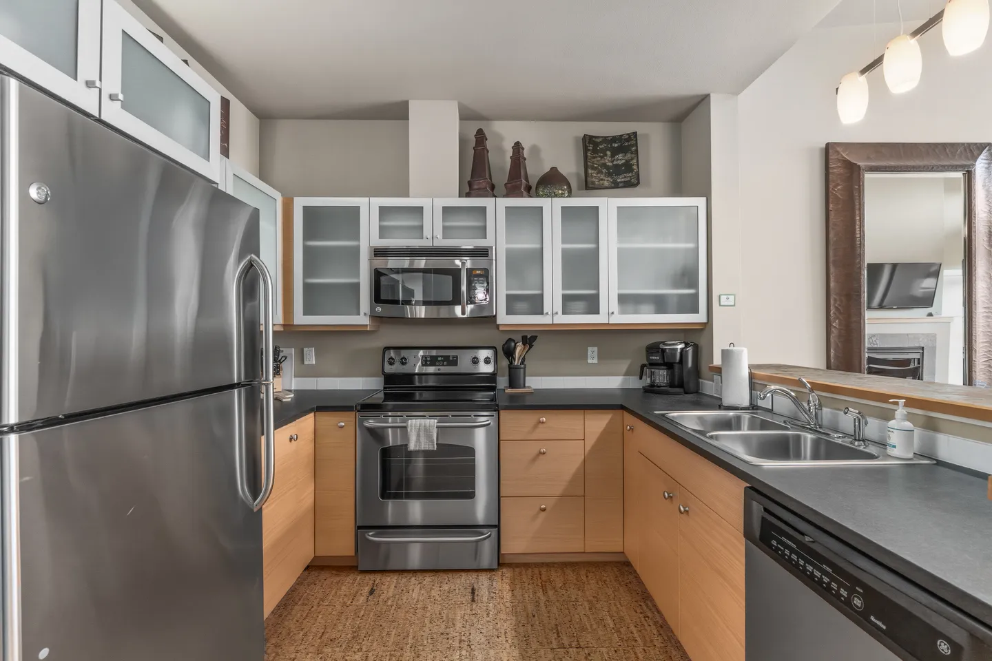 Kitchen with light wood lower cabinets, frosted glass upper cabinets, and stainless steel appliances.