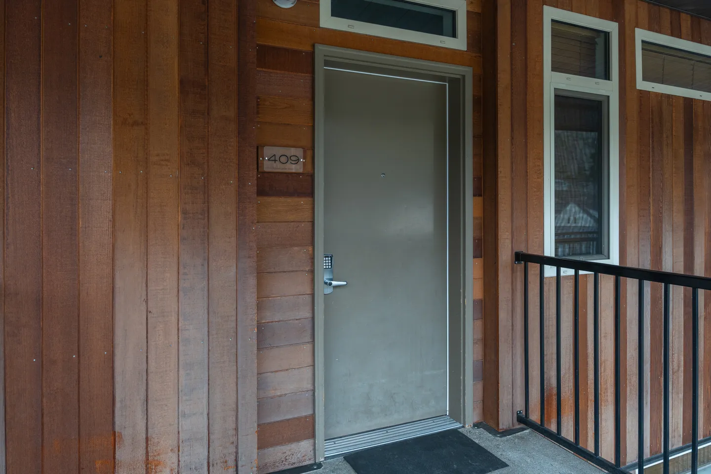 Exterior doorway with a gray entrance door, unit number 409 plaque, electronic keypad lock, and natural wood siding.