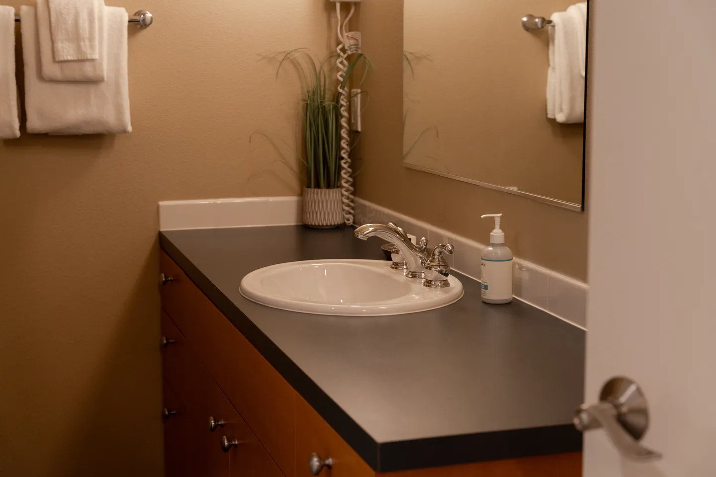 Bathroom vanity with a dark countertop, white oval drop-in sink, and wood-toned drawers.