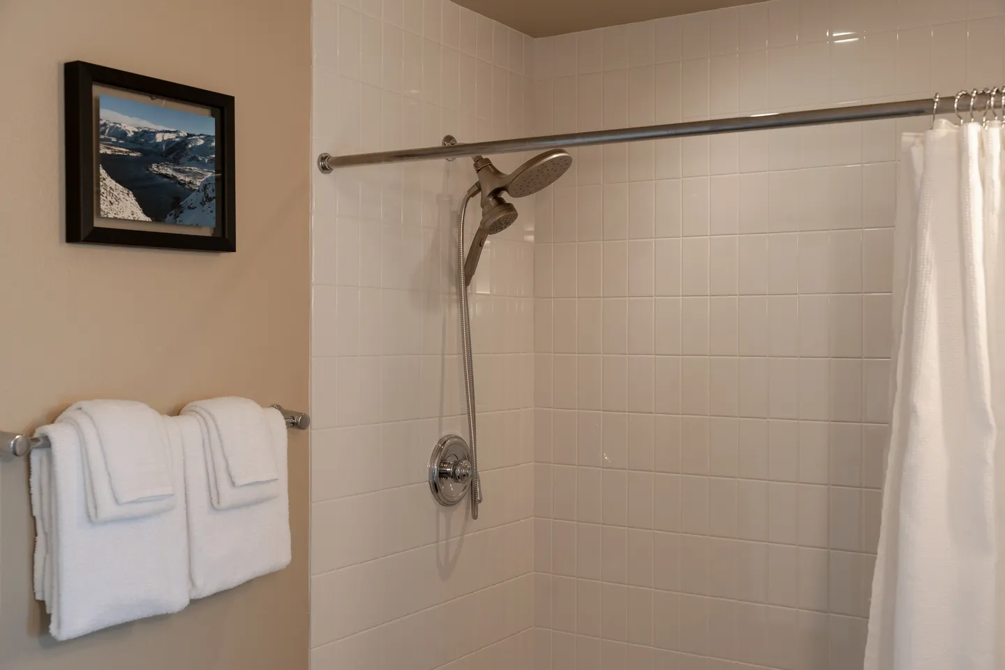 Bathroom shower with white square wall tiles, a handheld showerhead fixture, and folded white towels on a nearby rack.