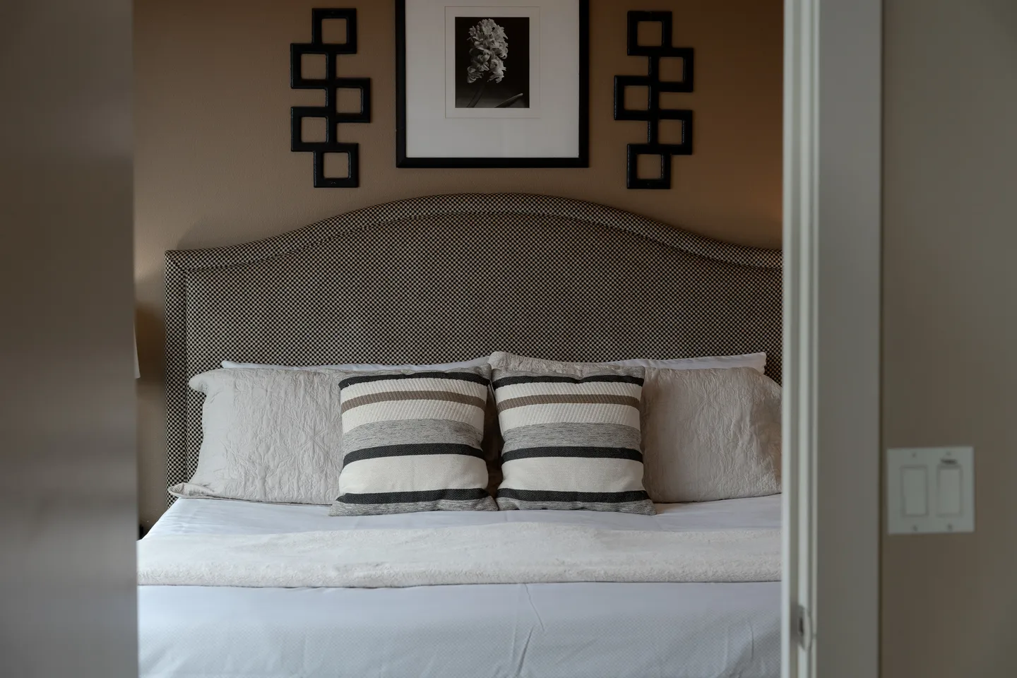 A made bed framed by a doorway, featuring a patterned arched headboard, striped accent pillows, and wall art above.