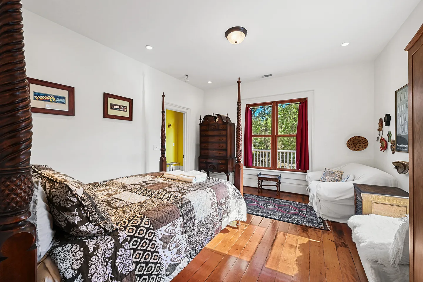 Bedroom featuring a four-poster wooden bed with a patterned quilt, wide-plank wood floors, a sofa, and an antique wooden cabinet.