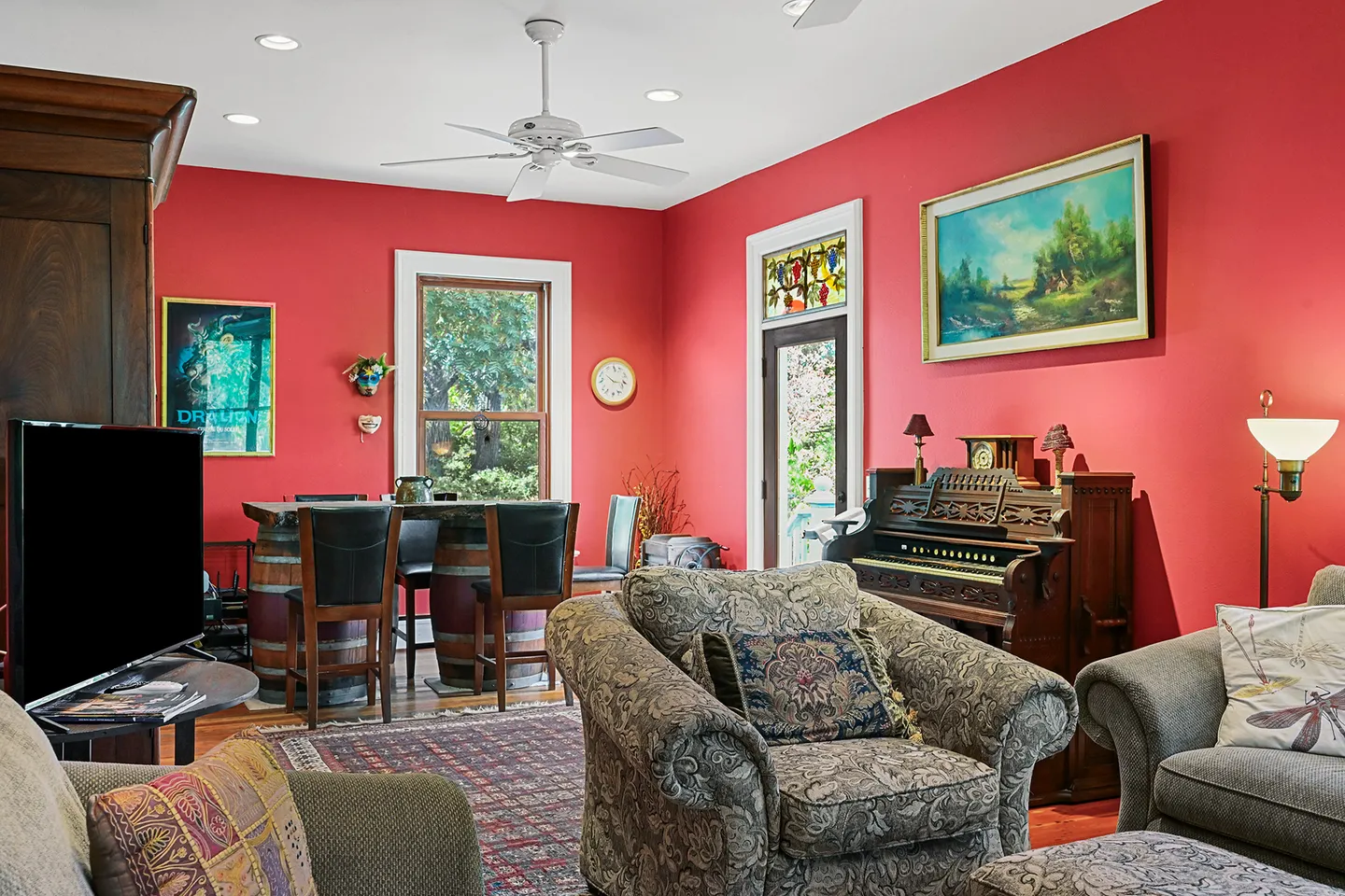 Living and entertainment room featuring vibrant red walls, plush armchairs, an organ, and a wine barrel bar table with stools.