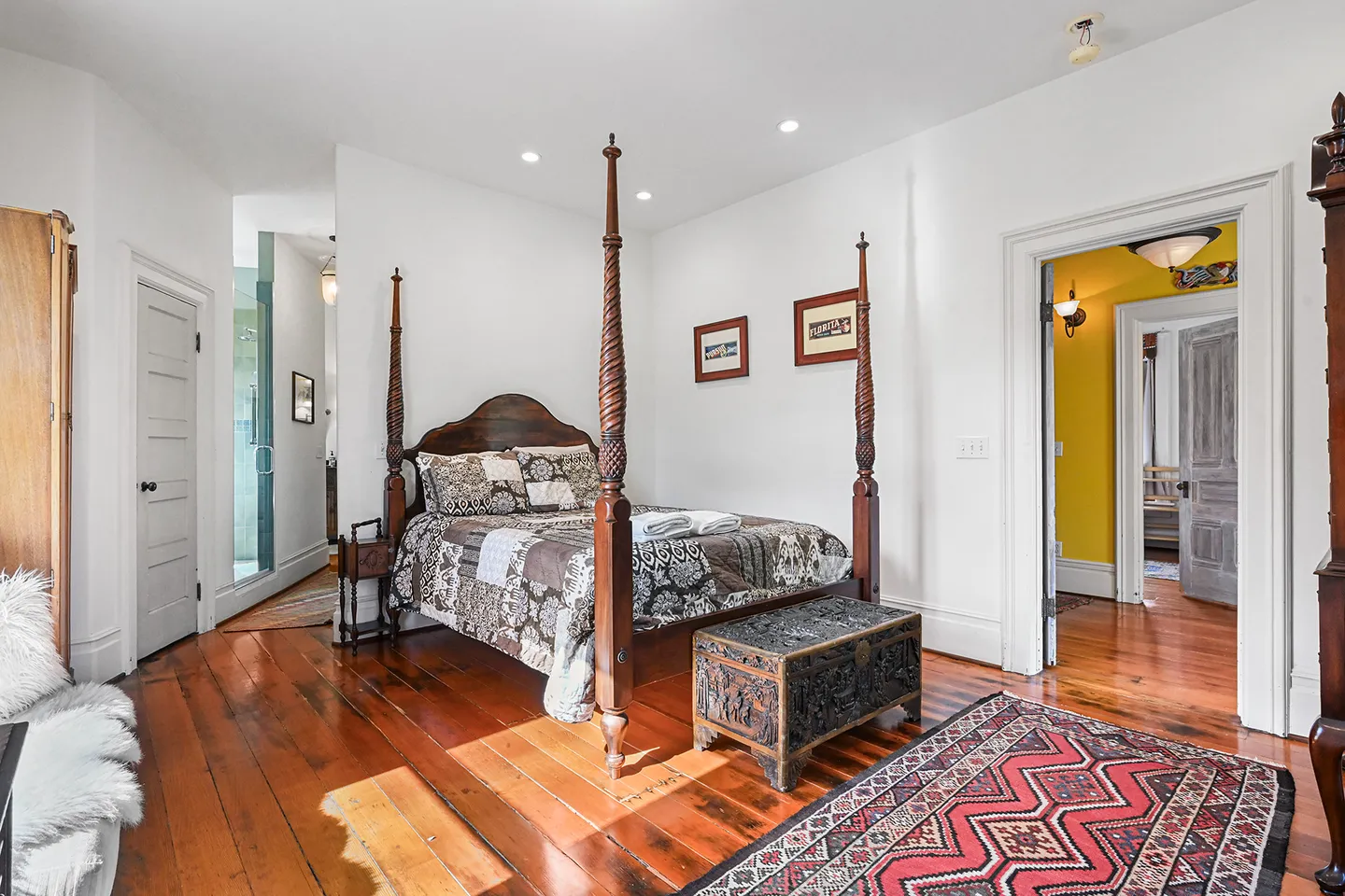 Bedroom featuring a carved four-poster wooden bed, polished wood floors, and doorways leading to a bathroom and hallway.