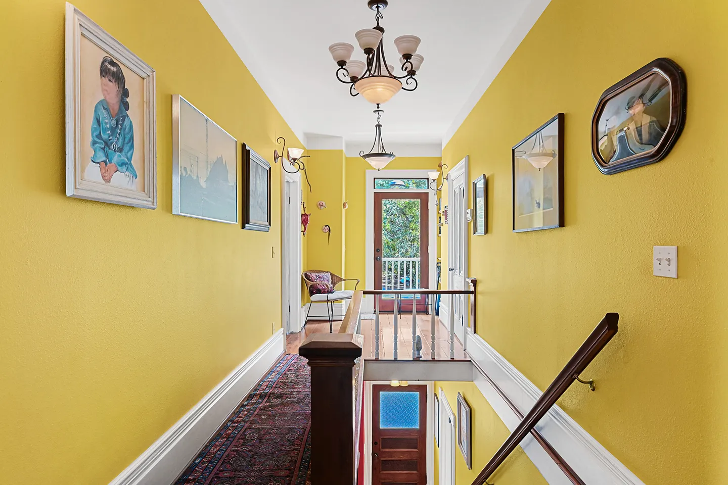 Upstairs hallway with yellow walls, framed art, chandelier lighting, and a view down the staircase.