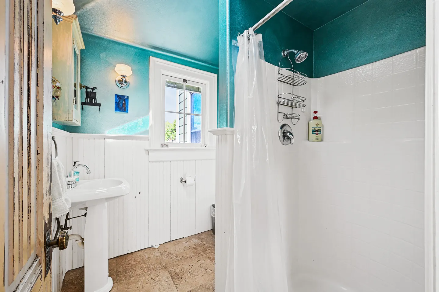 Bathroom with vibrant turquoise upper walls, white wainscoting, a pedestal sink, and a tiled shower stall with a curtain.