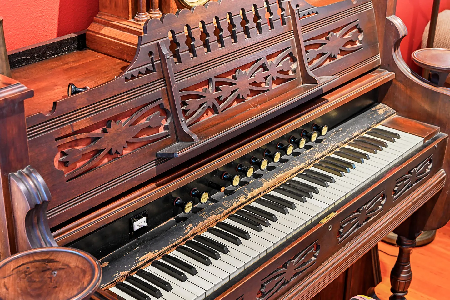 Close-up of a vintage dark wood pump organ with intricate fretwork and weathered keyboard stops.