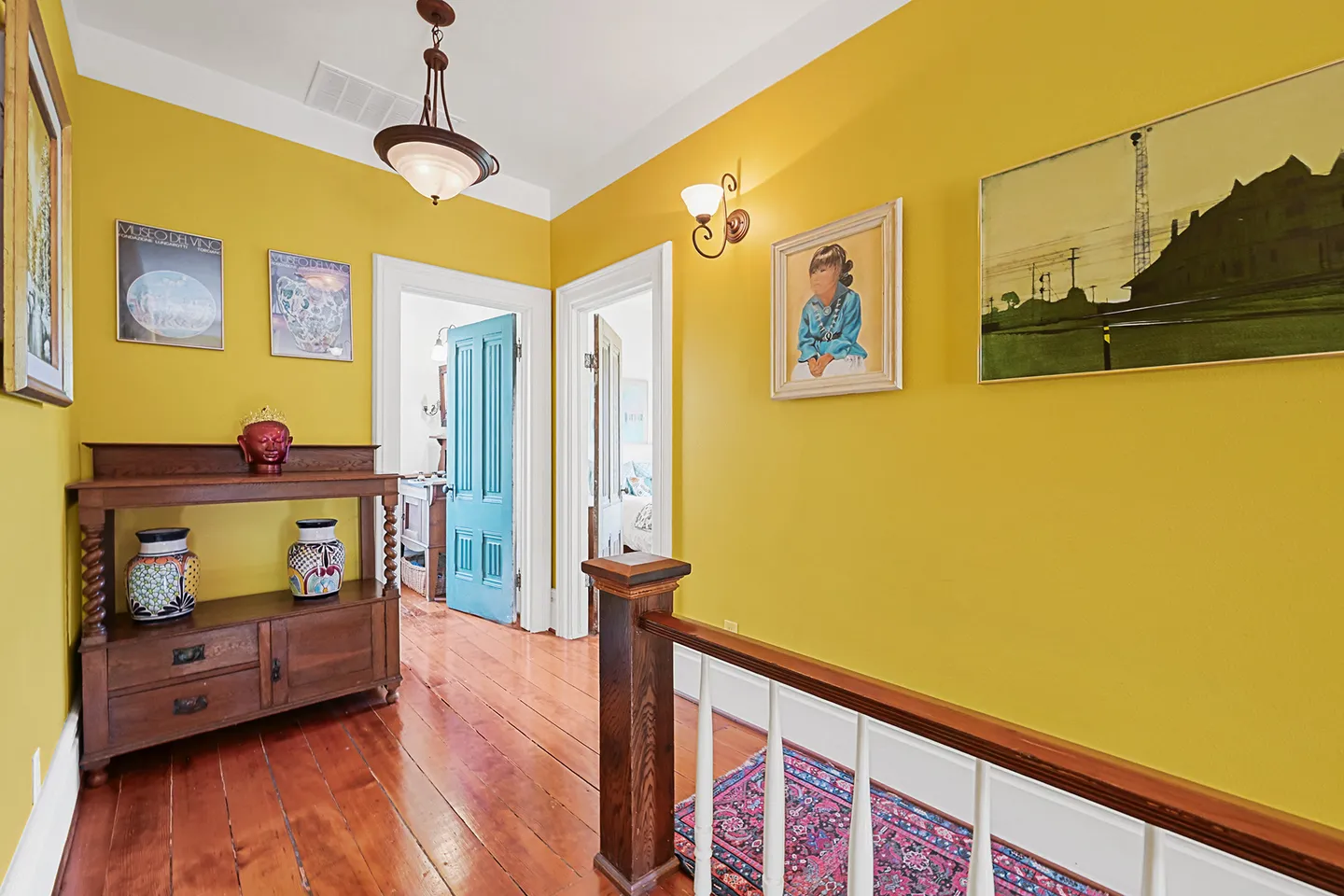 Upstairs hallway landing with bright yellow walls, wood flooring, a staircase railing, and framed artwork.