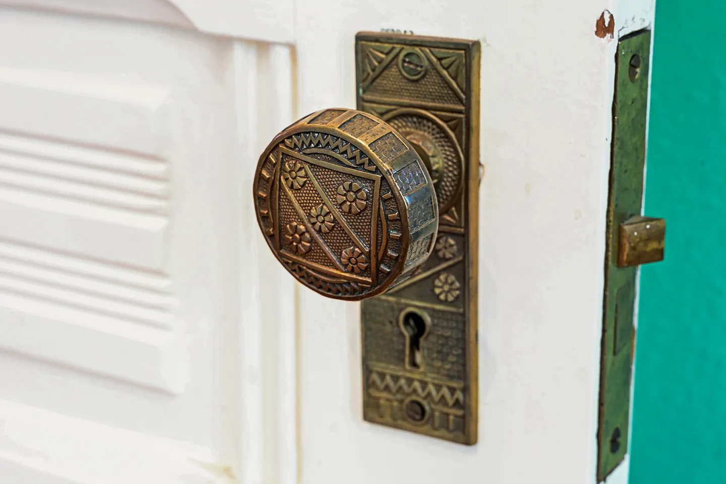 Close-up view of an antique patterned metal doorknob and matching backplate with a keyhole on a white paneled door.