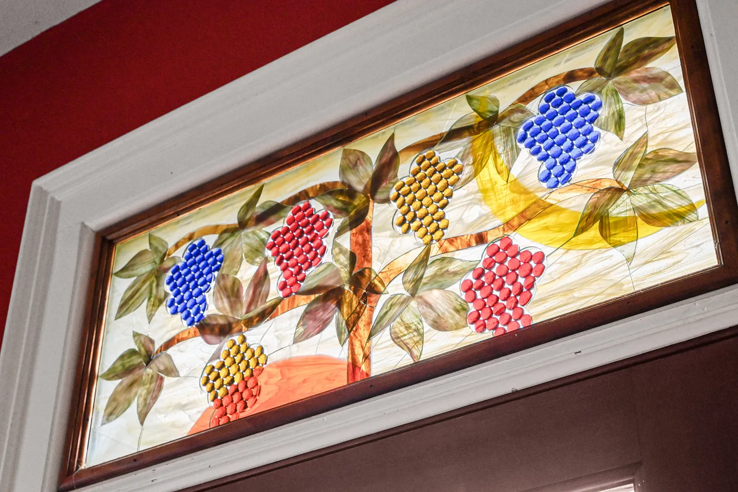 A close-up of a rectangular stained-glass transom window with a grape cluster motif above a door.