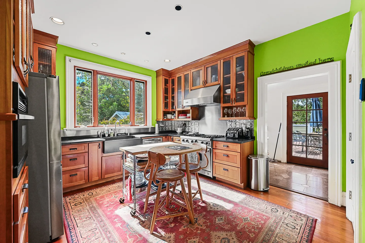 Bright kitchen featuring vivid green walls, warm wood cabinetry, stainless steel appliances, and a rolling kitchen island with stools.